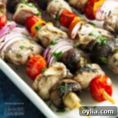 A close up of marinated chicken skewers  with tomatoes, red onions and mushrooms.