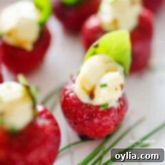 Creamy Brie Strawberry Bites 5 A close up photo of strawberries filled with whipped brie and topped with a basil leaf.