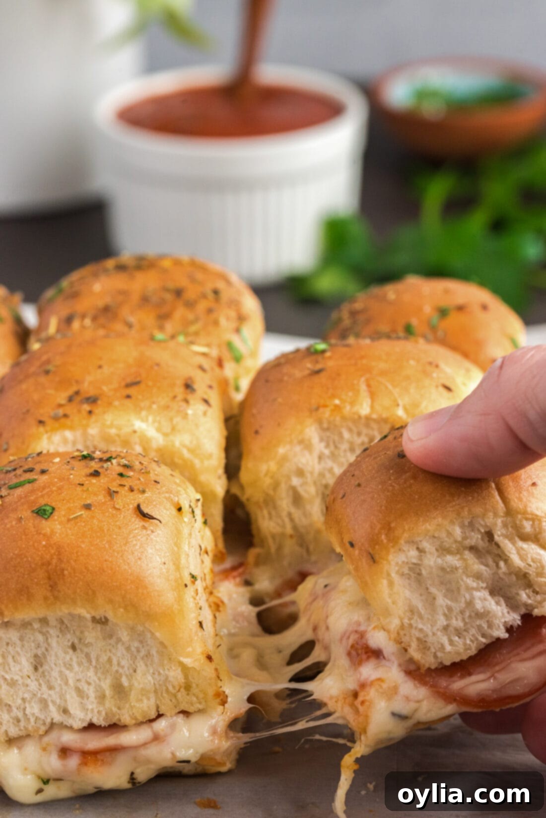 Hand pulling a melted cheese pizza slider from a baking dish