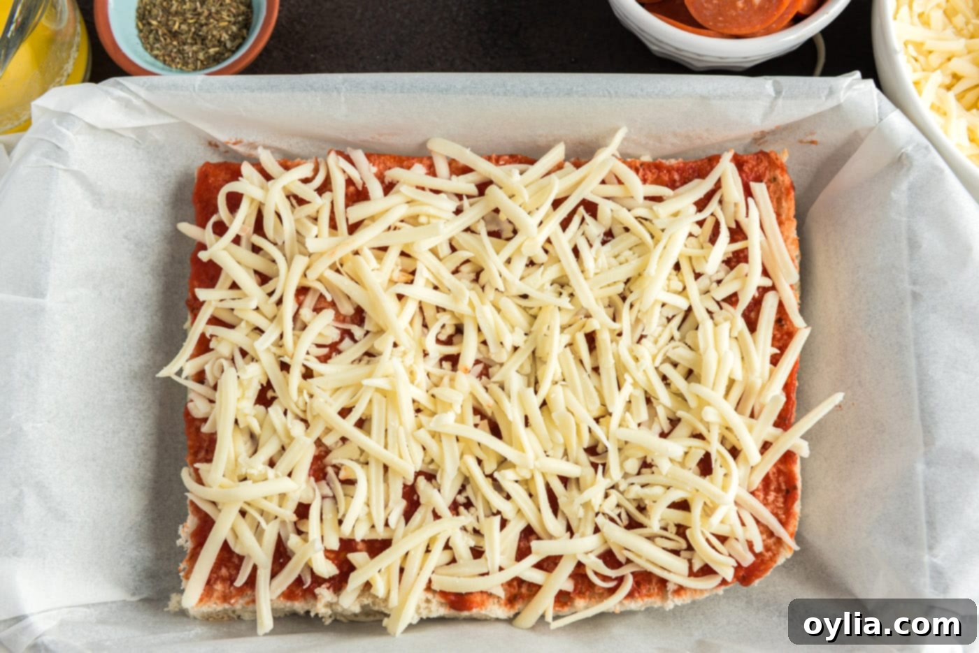 First layer of shredded mozzarella cheese covering the pizza sauce on slider buns