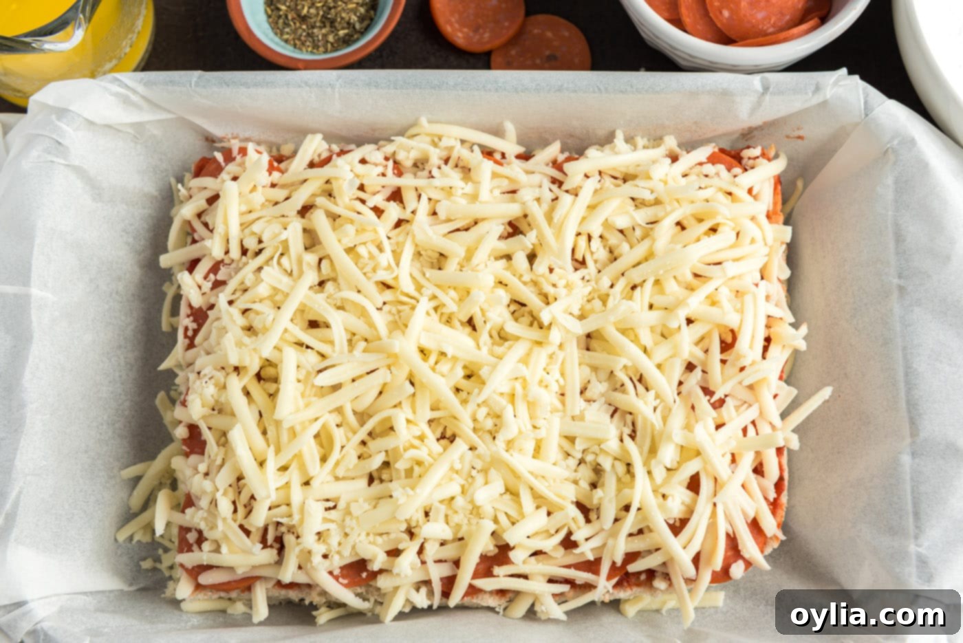 Second layer of shredded mozzarella cheese covering pepperoni slices on pizza sliders