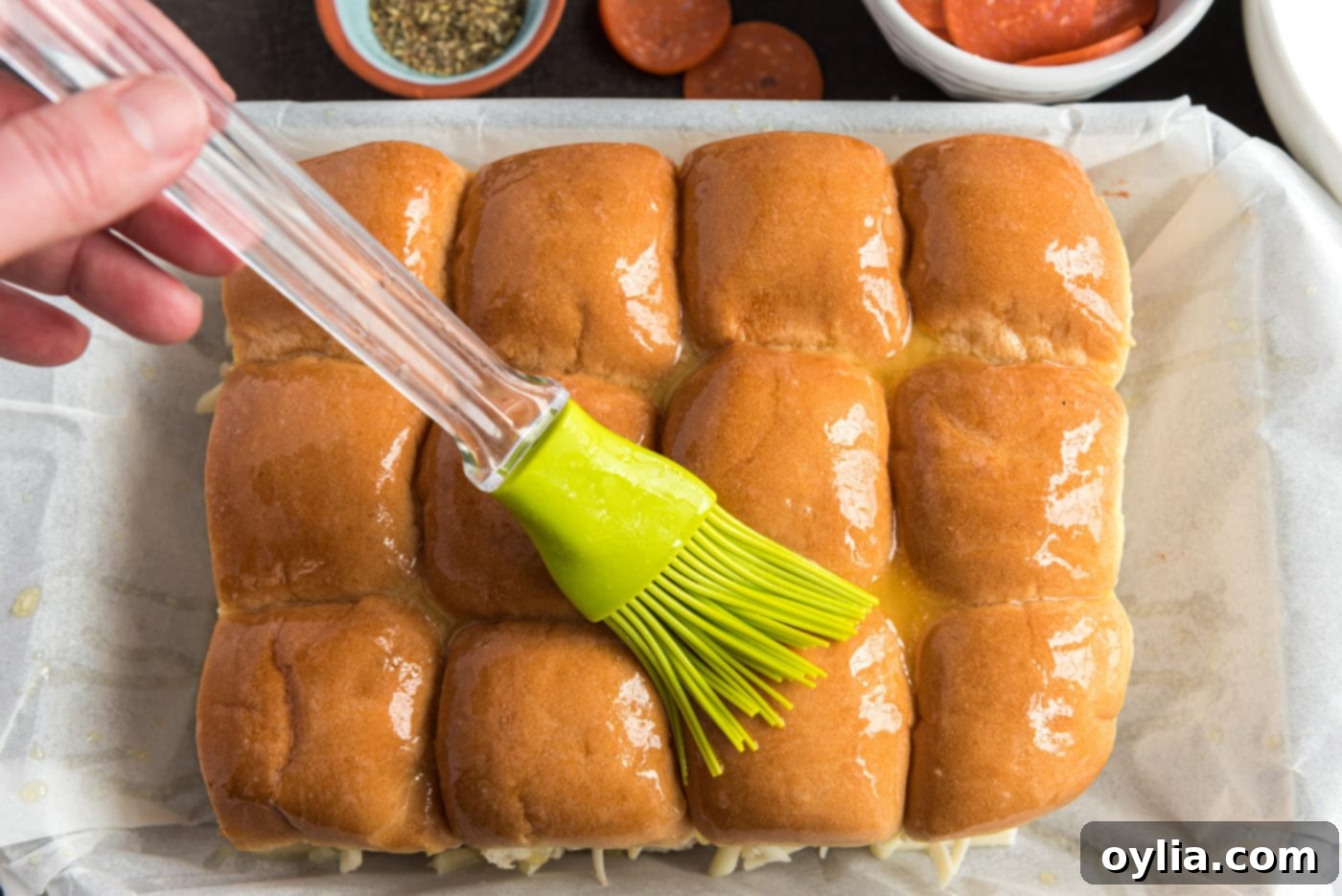 Basting the tops of assembled pizza slider buns with melted butter