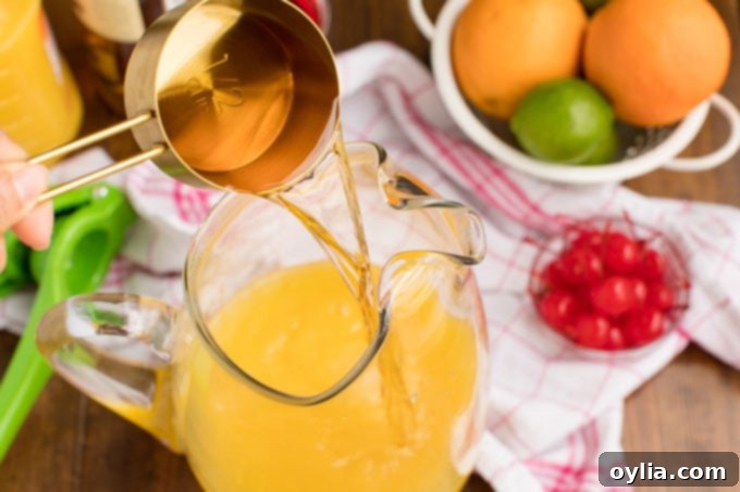 Pouring dark rum into a pitcher filled with a mix of orange and pineapple juices, starting the rum punch creation.