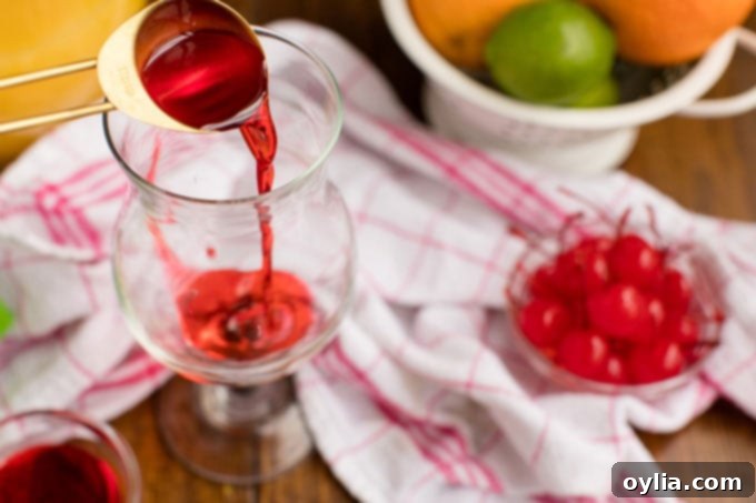 Adding a tablespoon of vibrant red grenadine syrup to the bottom of a hurricane glass, setting the stage for the layered effect.