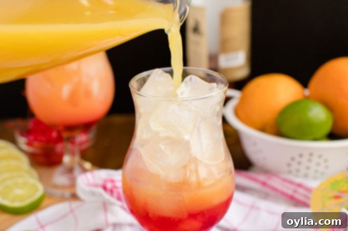 Slowly pouring the mixed rum punch into a glass, creating a beautiful sunset gradient effect with the grenadine at the bottom.
