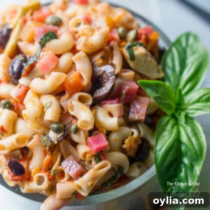 A close up of a bowl filled with Mediterranean pasta salad and a basil leaf on the side.