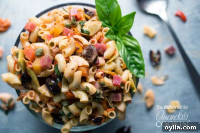 A close up of a bowl filled with Mediterranean pasta salad and a basil leaf on the side.
