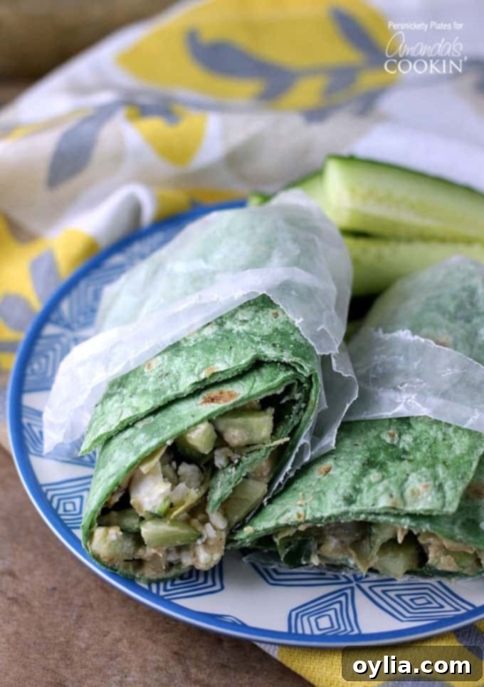 Two halves of a Mediterranean veggie wrap in wax paper resting next to each other on a blue and white plate. This image highlights the fresh ingredients and the appealing presentation.