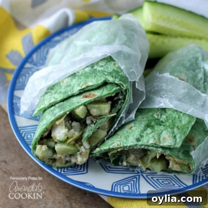 Two halves of a Mediterranean veggie wrap in wax paper resting next to each other on a blue and white plate. This close-up shows the colorful fillings peeking out, emphasizing its freshness.