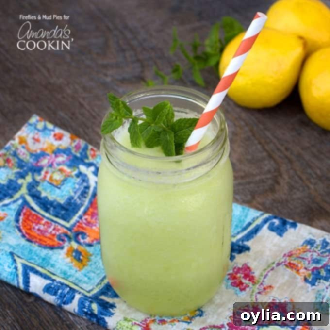 A close-up view of a mason jar filled with the refreshing honeydew lemon slush, adorned with a sprig of fresh mint and a festive red and white striped straw, ready to be enjoyed.
