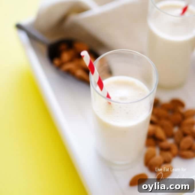 An overhead of a tall clear glass filled with an almond maple smoothie and served with a red and white straw.
