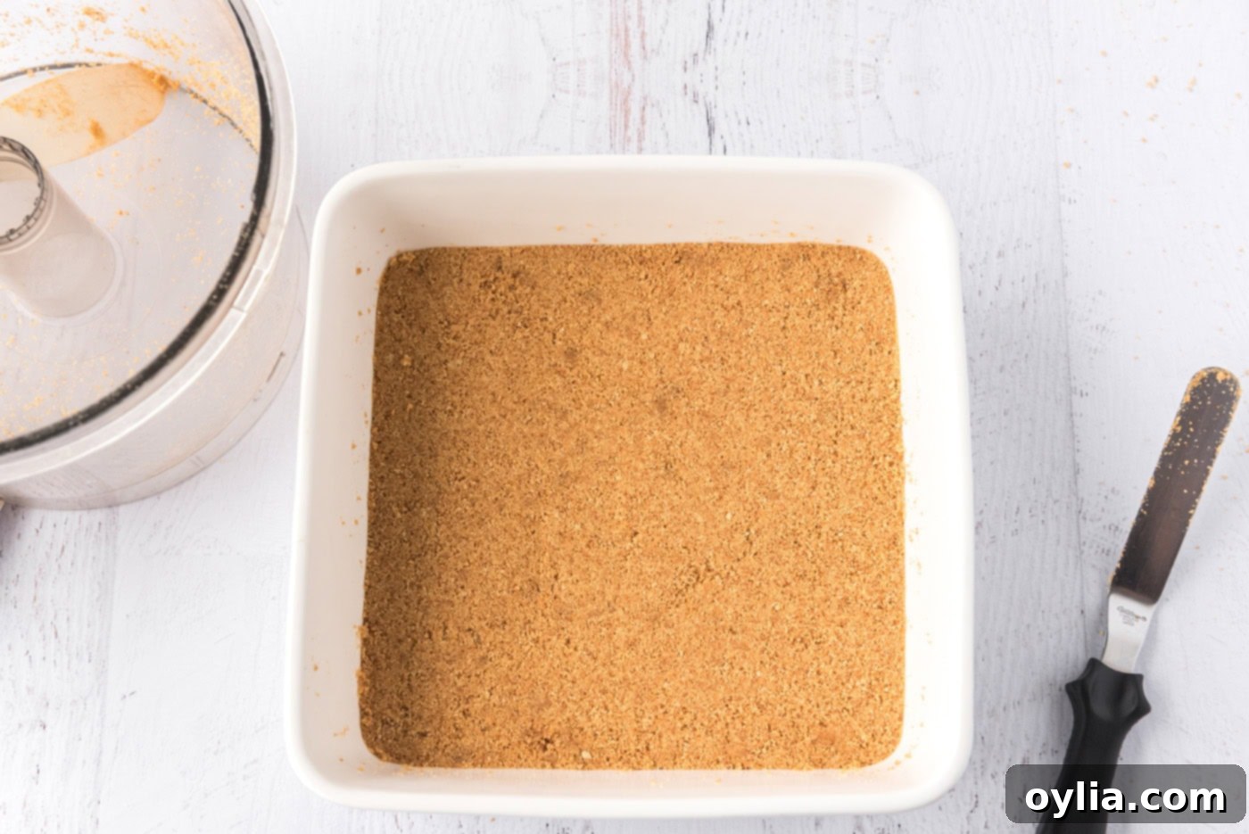 Buttery graham cracker crust pressed evenly into a square baking pan, ready for the filling