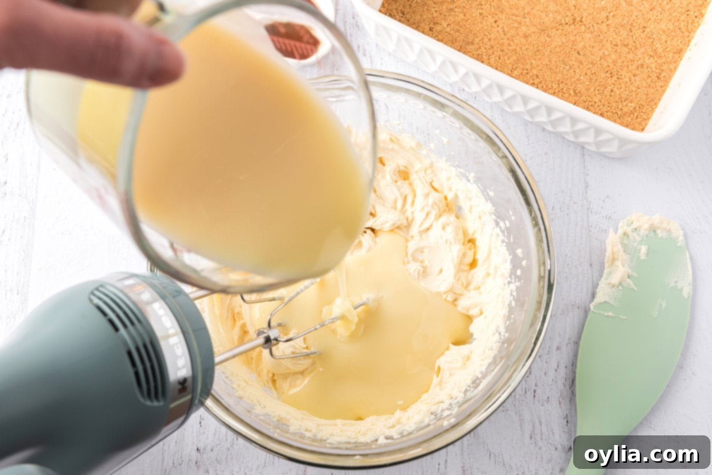 Pouring sweetened condensed milk into fluffy mascarpone cheese mixture with a handheld mixer