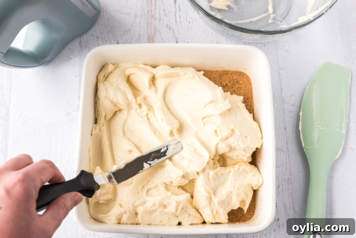 Spreading smooth mascarpone cheesecake filling over a graham cracker crust in a square pan