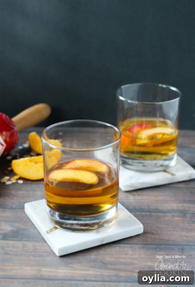 Two short clear glasses filled with peach pie cocktail with two peach slices floating on top, ready to be enjoyed.