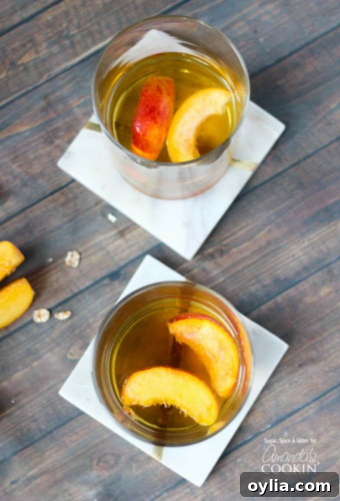 An overhead view of two short clear glasses filled with a vibrant peach pie cocktail, garnished with two peach slices floating elegantly on top, suggesting a refreshing and flavorful experience.