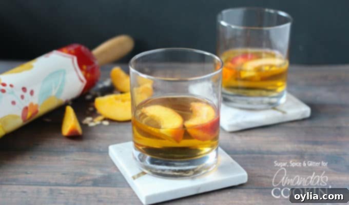 Two clear short glasses showcasing a golden peach pie cocktail, with peach slices gracefully floating on top, presented on a simple surface, ready for a horizontal close-up shot.