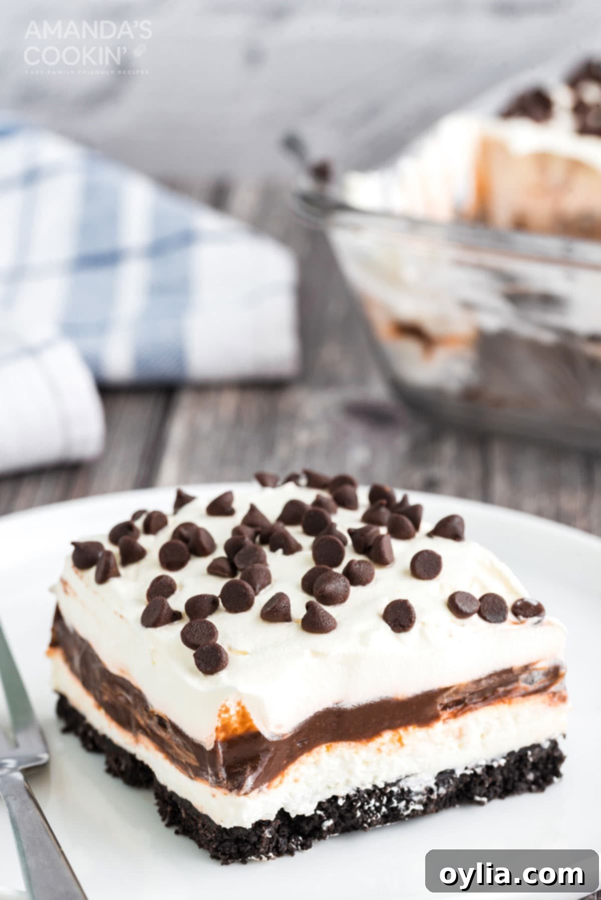 Chocolate lasagna is a no-bake layered dessert made with cookies, cream cheese, whipped cream and chocolate pudding. It's a chocolate dessert dream! slice of chocolate lasagna on a white plate, showcasing its distinct layers