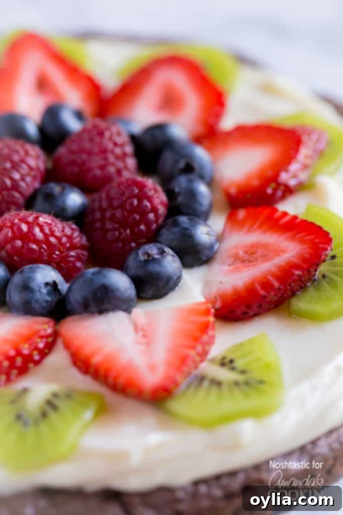 A close up of cut up strawberries, kiwi, blueberries and raspberries on a brownie pizza.