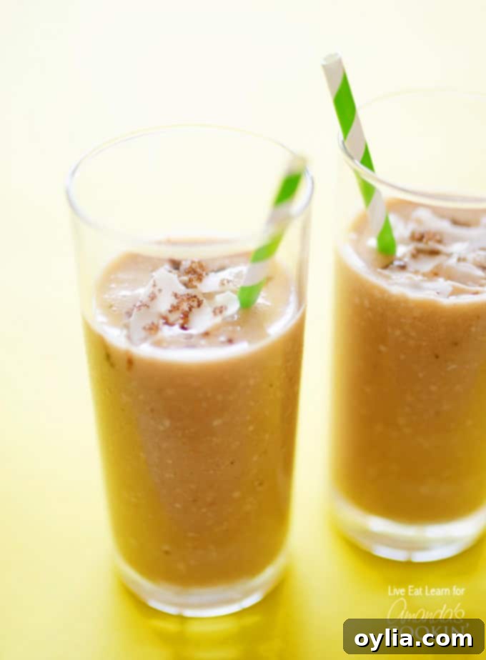A close up of two tall clear glasses filled with cozy coconut smoothie and served with a green and white striped straw.