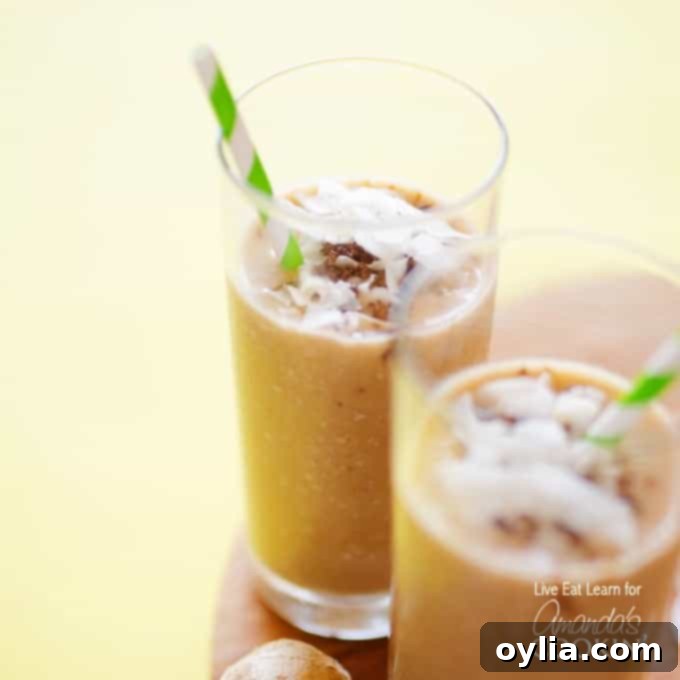 Two tall clear glasses filled with a cozy coconut smoothie and served with a green and white striped straw.