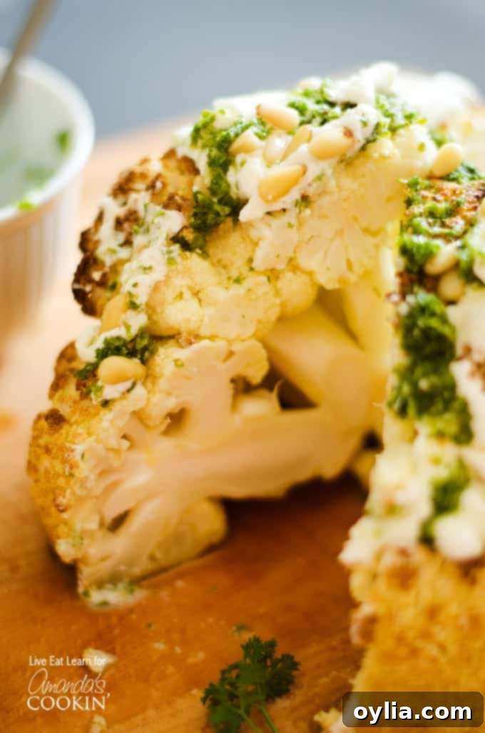 A close up of the center of a whole roasted cauliflower topped with whipped feta and herb sauce on a wooden cutting board.