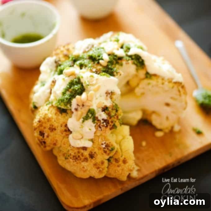 A close up of a whole roasted cauliflower topped with whipped feta and herb sauce on a wooden cutting board.