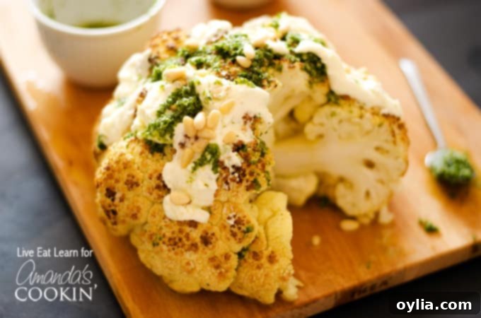 A close up of a whole roasted cauliflower topped with whipped feta and herb sauce on a wooden cutting board.