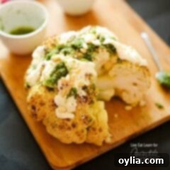 Simply Perfect Whole Roasted Cauliflower 6 A close up of a whole roasted cauliflower topped with whipped feta and herb sauce on a wooden cutting board.