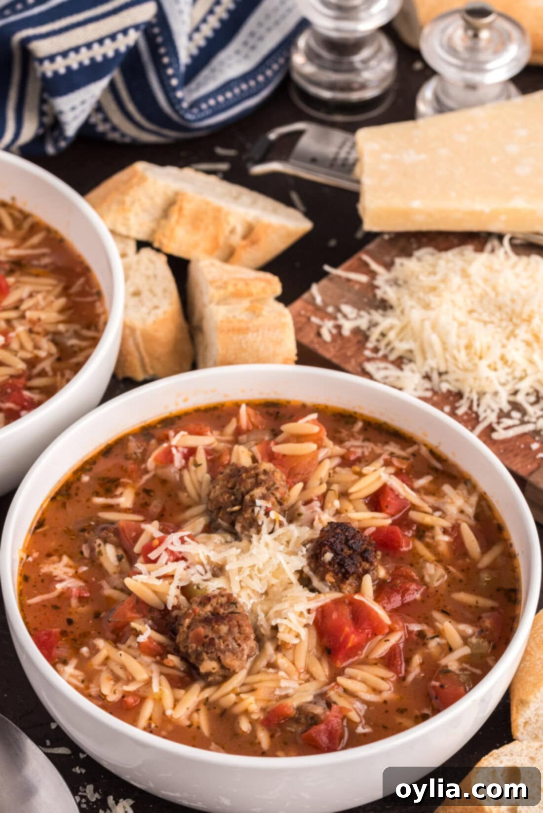 Hearty Sausage and Orzo Soup 2 Two bowls of Italian Sausage Tomato Orzo Soup with bread and cheese in the background