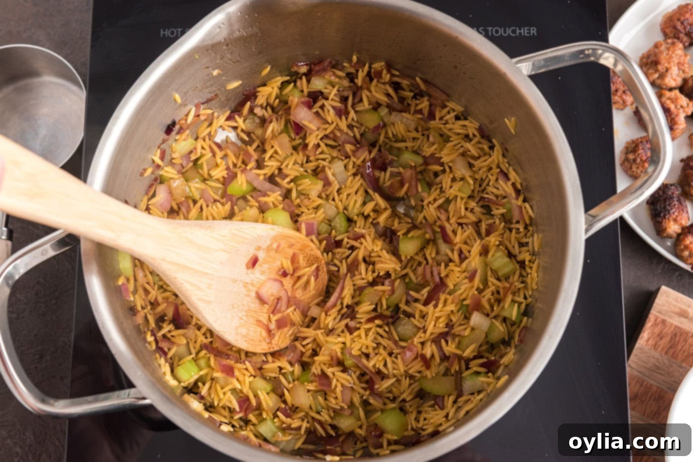 wooden spoon in a pot with orzo, sausage, and veggies