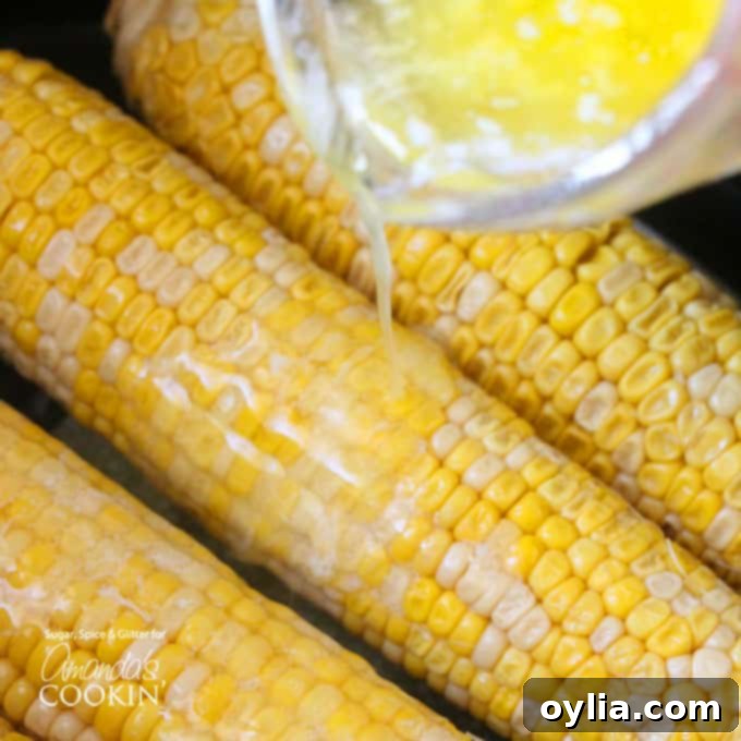 An overhead shot of melted butter being generously poured over cooked corn on the cob.