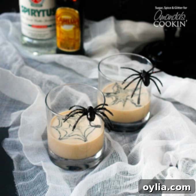 Two clear glasses filled with a spiderweb in cream martini and a fake spider on the glass.
