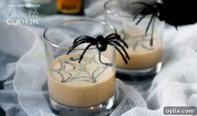 A close up of two clear glasses filled with a spiderweb in cream martini and a fake spider on the glass.