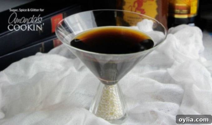 A clear martini glass filled with a raven coffee cocktail, on a dark surface.