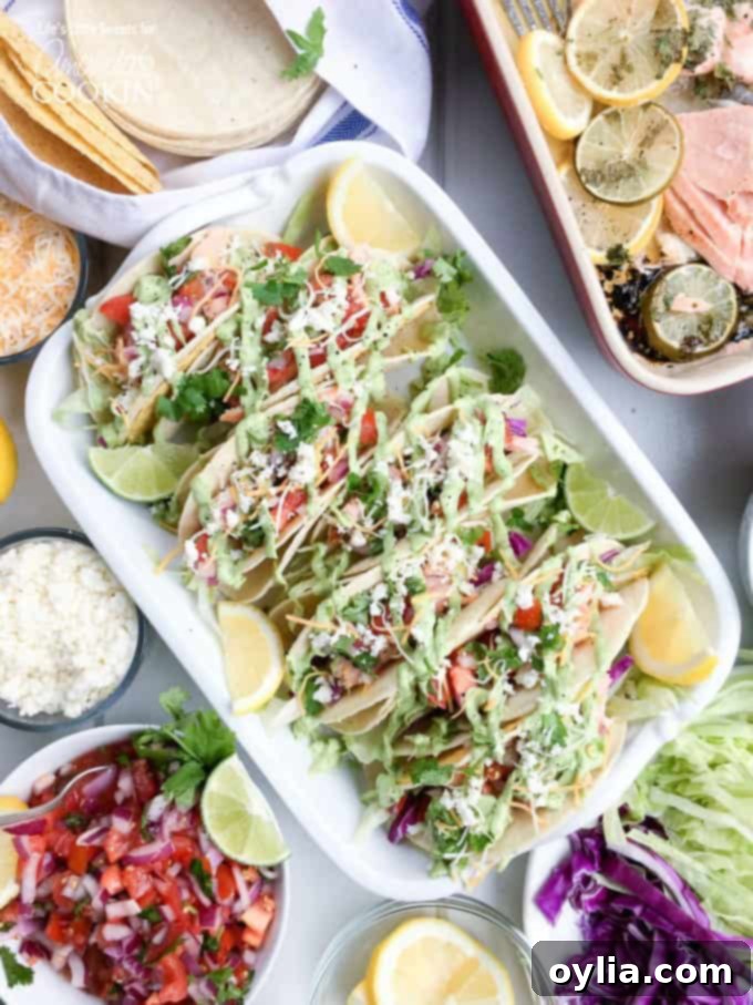 An overhead photo of four vibrant salmon tacos, generously filled with flaked salmon, fresh salsa, and creamy avocado sauce, resting in a casserole dish with lemon and lime wedges on the side, ready to be enjoyed.