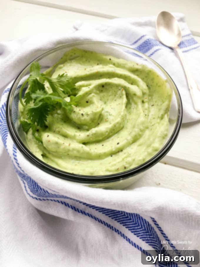 A close-up photo of a creamy, vibrant green bowl of homemade avocado sauce, garnished with fresh cilantro, ready to top salmon tacos.