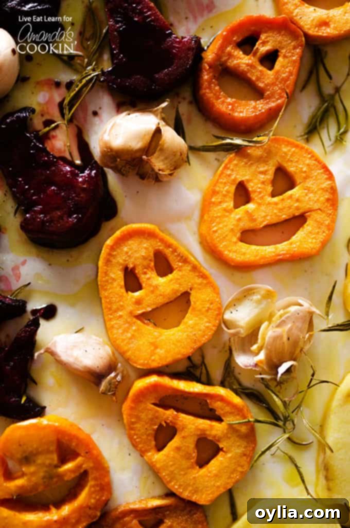 A close up overhead photo of roasted Halloween vegetables artfully arranged on a white platter, featuring carved sweet potato jack-o-lanterns, beet witch's hats, and potato ghosts, all seasoned and perfectly roasted.