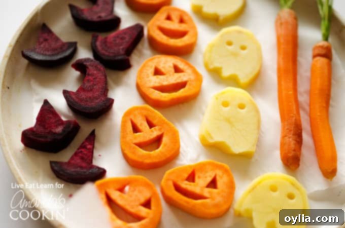 A horizontal close up photo of roasted Halloween vegetables, showcasing the variety of shapes and vibrant colors, seasoned with herbs and garlic.