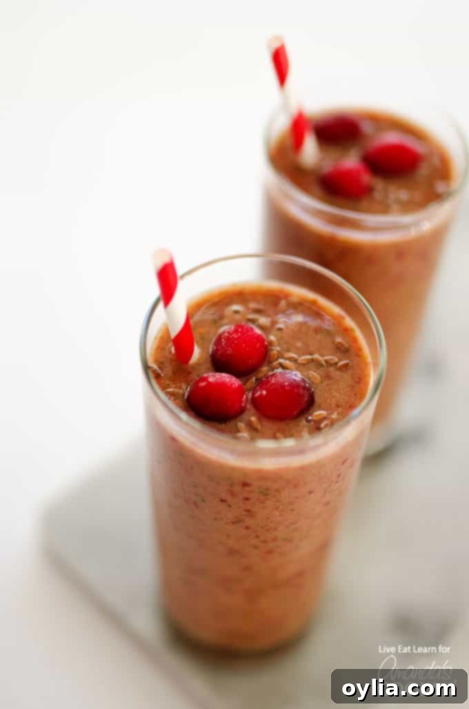 A close up overhead of two cranberry smoothies with cranberries on top and served with a straw, showcasing a vibrant red color.