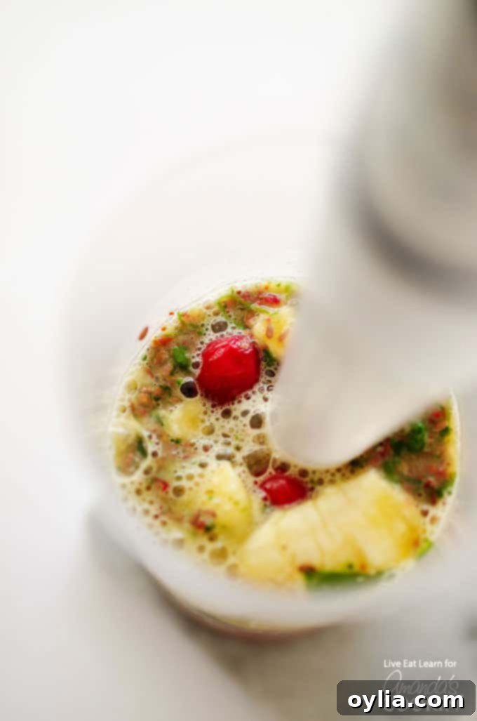 A close up photo of a vibrant cranberry smoothie being blended with an immersion blender in a large glass jar.