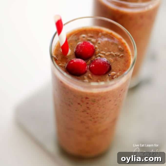 A vibrant Cranberry Smoothie in a tall glass with a straw and fresh cranberries on top.