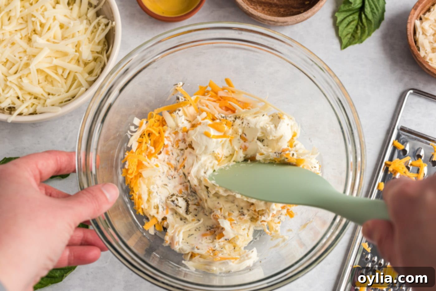 mixing cream cheese, cheddar, mozzarella, and herbs in a bowl for pizza dip base