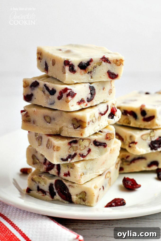 Squares of creamy white chocolate cranberry fudge, richly studded with red cranberries and brown pecans, stacked invitingly on top of each other.
