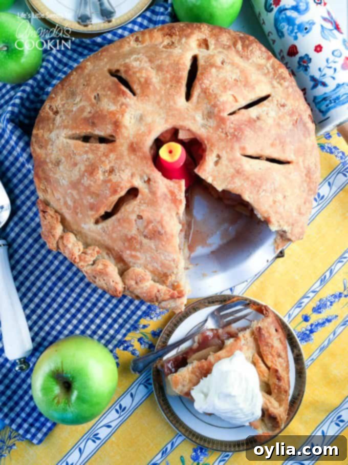 A whole homemade apple pie with a missing slice that is sitting on a plate to the side, highlighting the golden-brown crust and juicy filling.
