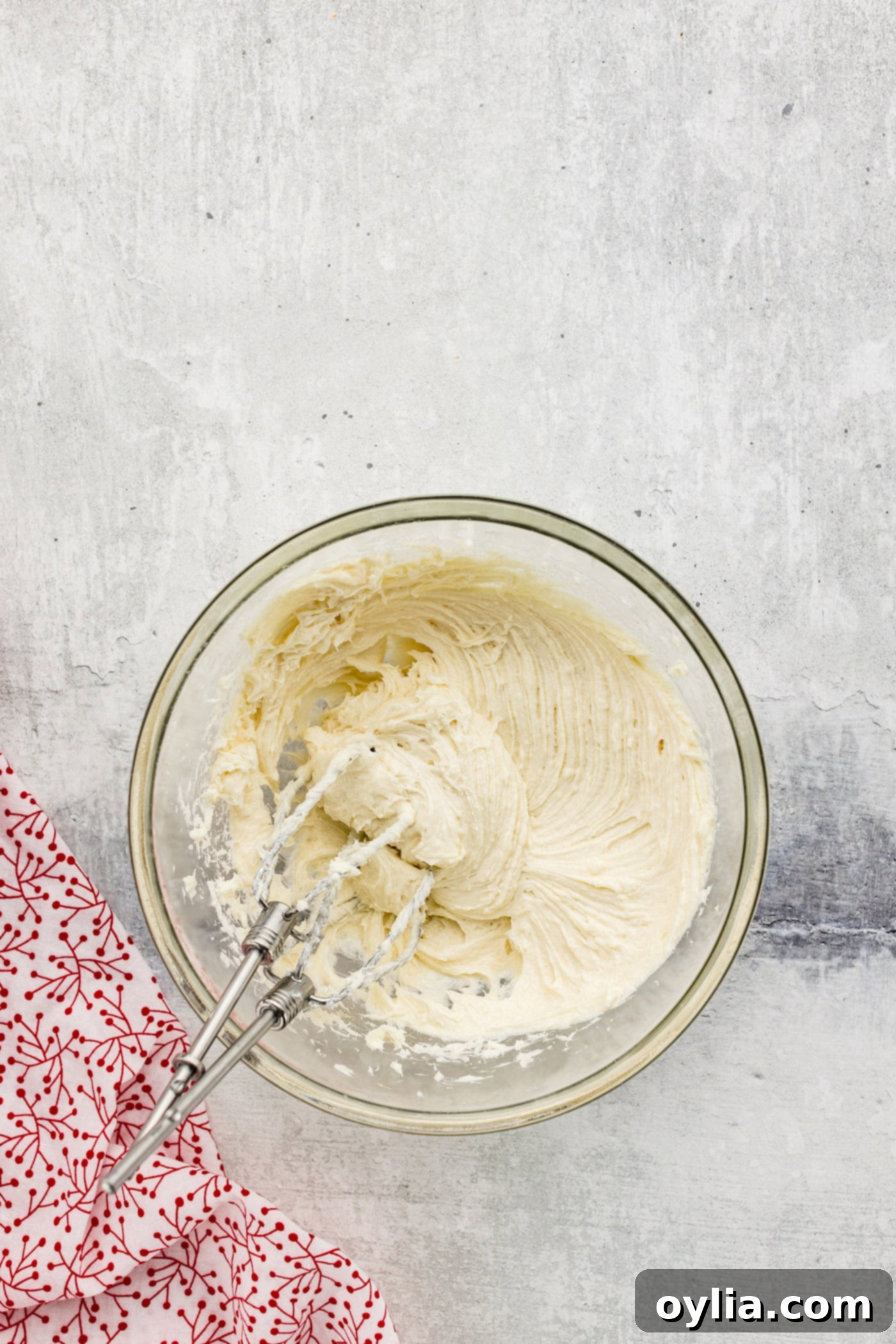 Cream cheese, sugar, and vanilla being beaten with a hand mixer in a bowl until smooth