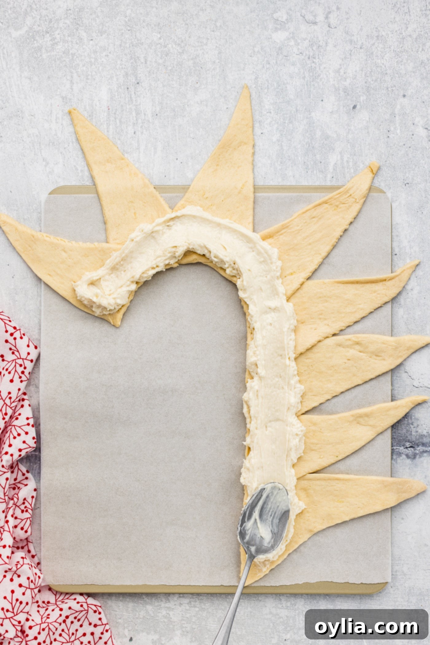 Spreading cream cheese filling inside the crescent roll dough shaped as a candy cane