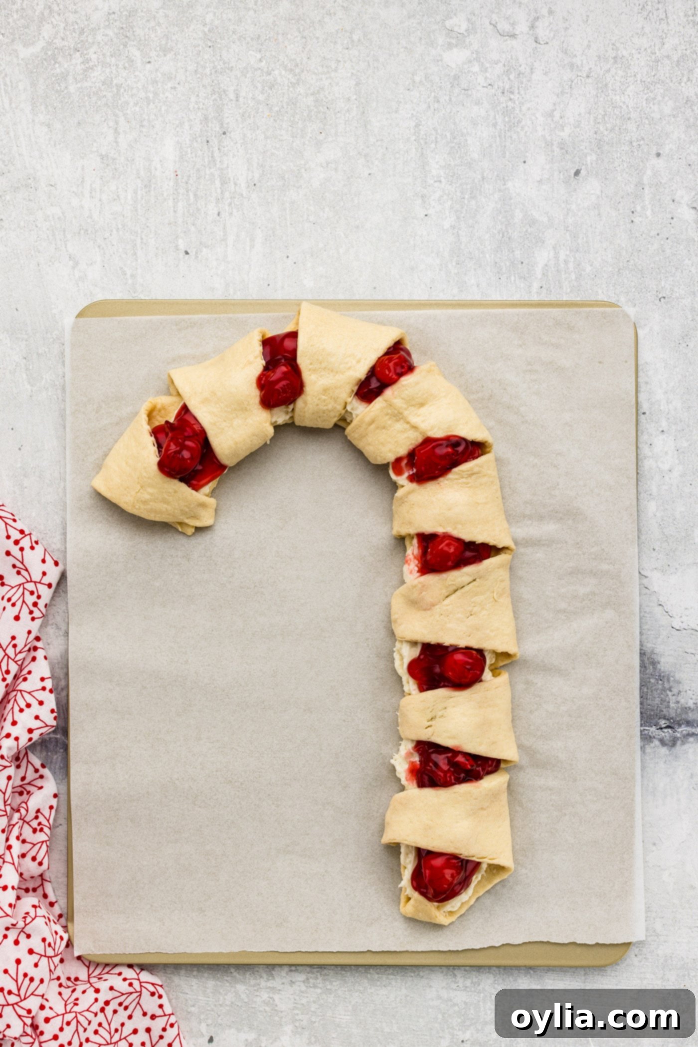 Assembling a cherry candy cane danish by folding crescent roll points to form stripes