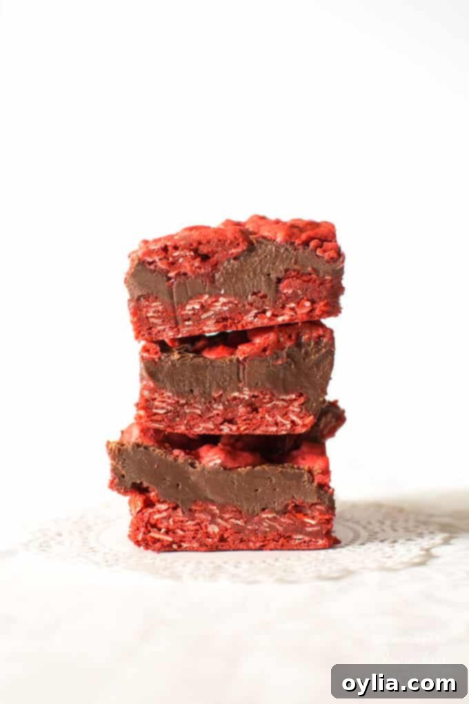 Three squares of decadent Red Velvet Oatmeal Fudge Bars stacked on top of each other, showcasing the vibrant red cookie layers and rich fudge center.