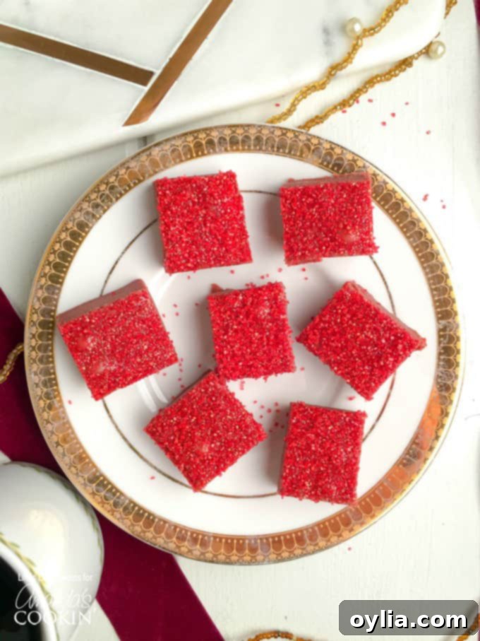 Squares of red velvet fudge with red sprinkles on top sitting on a white and gold plate.